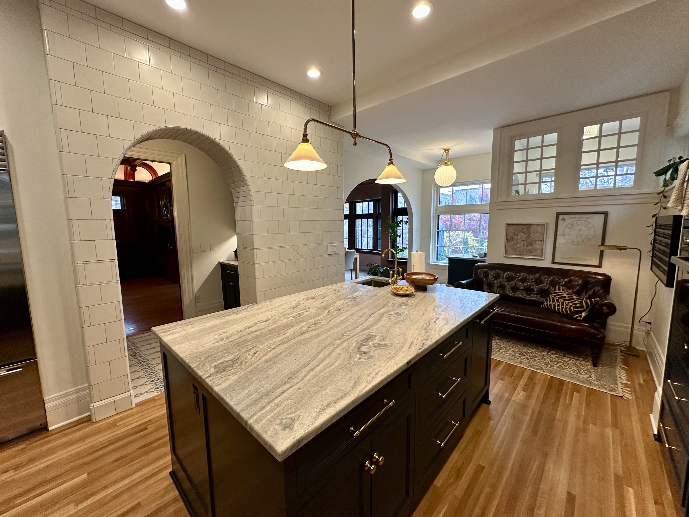Chef's kitchen with marble island, brass pendant lights, and an arched doorway to the breakfast nook.