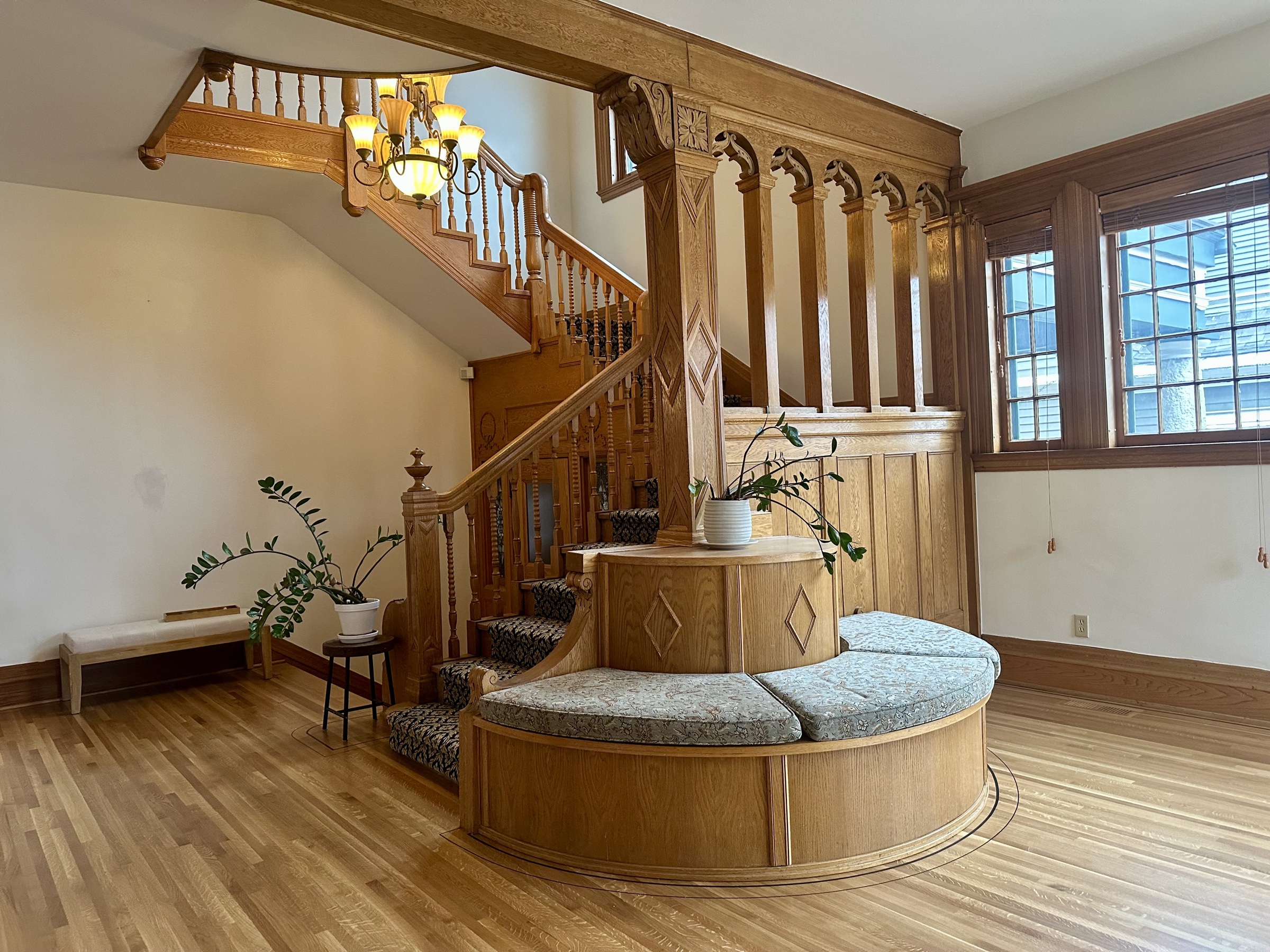 The grand staircase and round foyer banquette at 638 Summit Avenue, with morning light through the leaded-glass overhead.